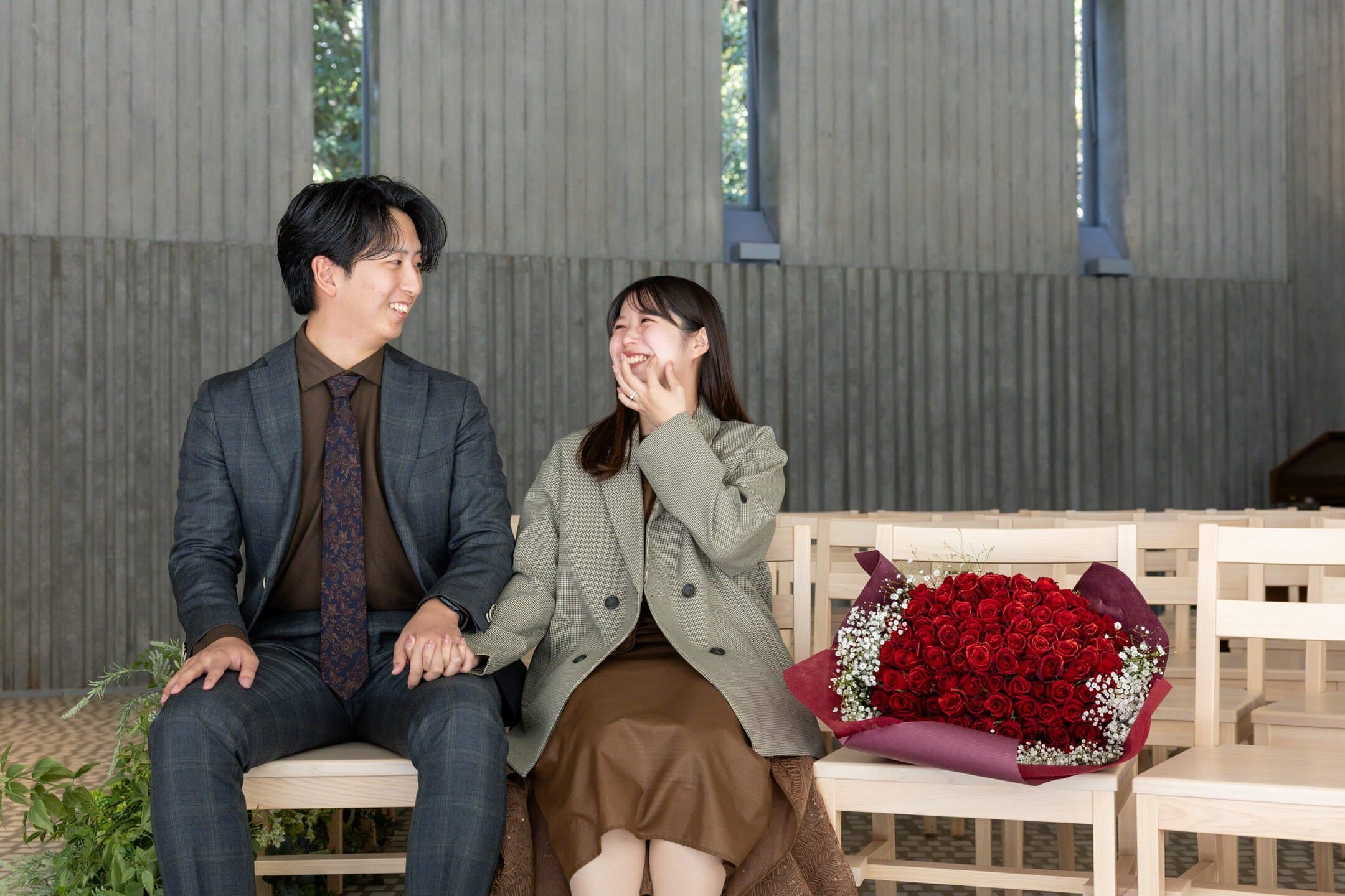 幸せなカップルがプロポーズ後に座っているシーン、花束を持ち笑顔で喜び合う瞬間を室内で撮影した写真です。.