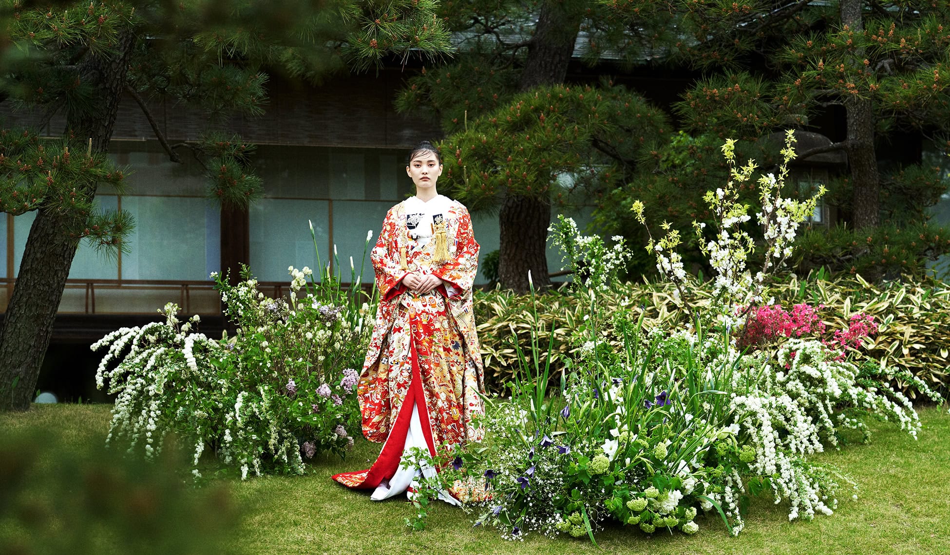 伝統的な着物を着た女性が庭園でポーズをとる、華やかな和装の結婚式シーン.