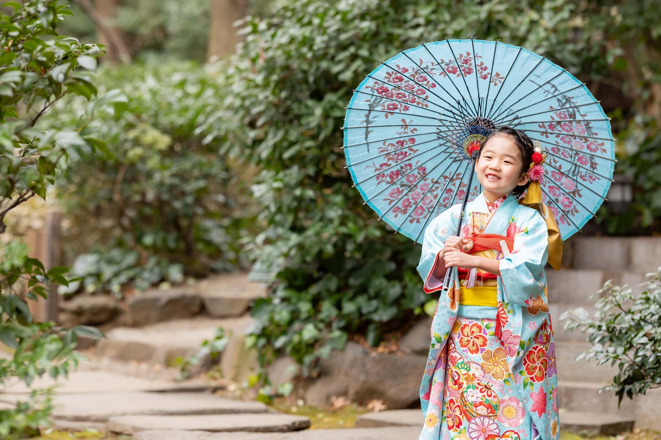 伝統的な着物を着た少女が庭園で和傘を持ち笑顔で立つ風景.