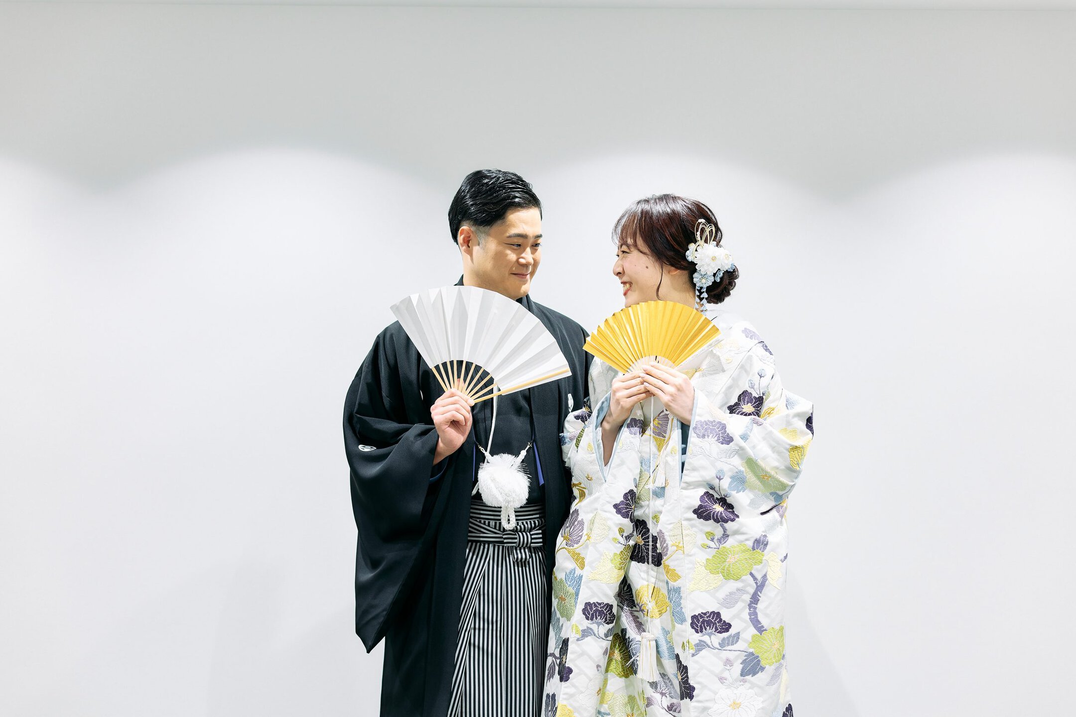 伝統的な和装の新郎新婦が扇子を持ち笑顔で見つめ合う結婚式の写真.