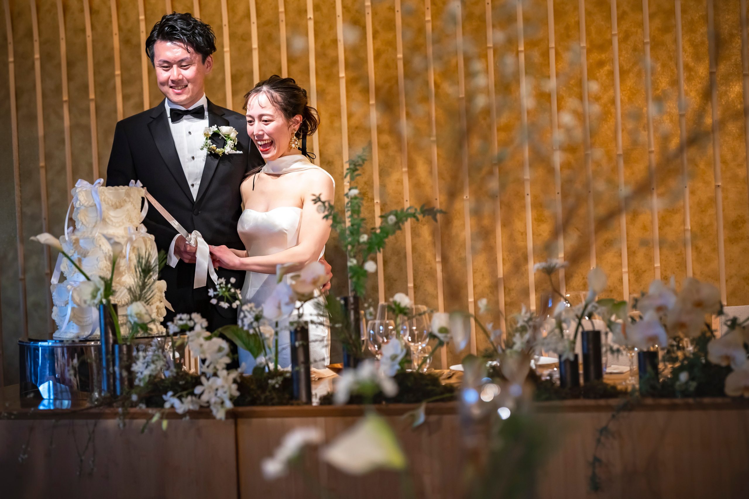 笑顔でウエディングケーキ入刀のセレモニーをする新郎新婦