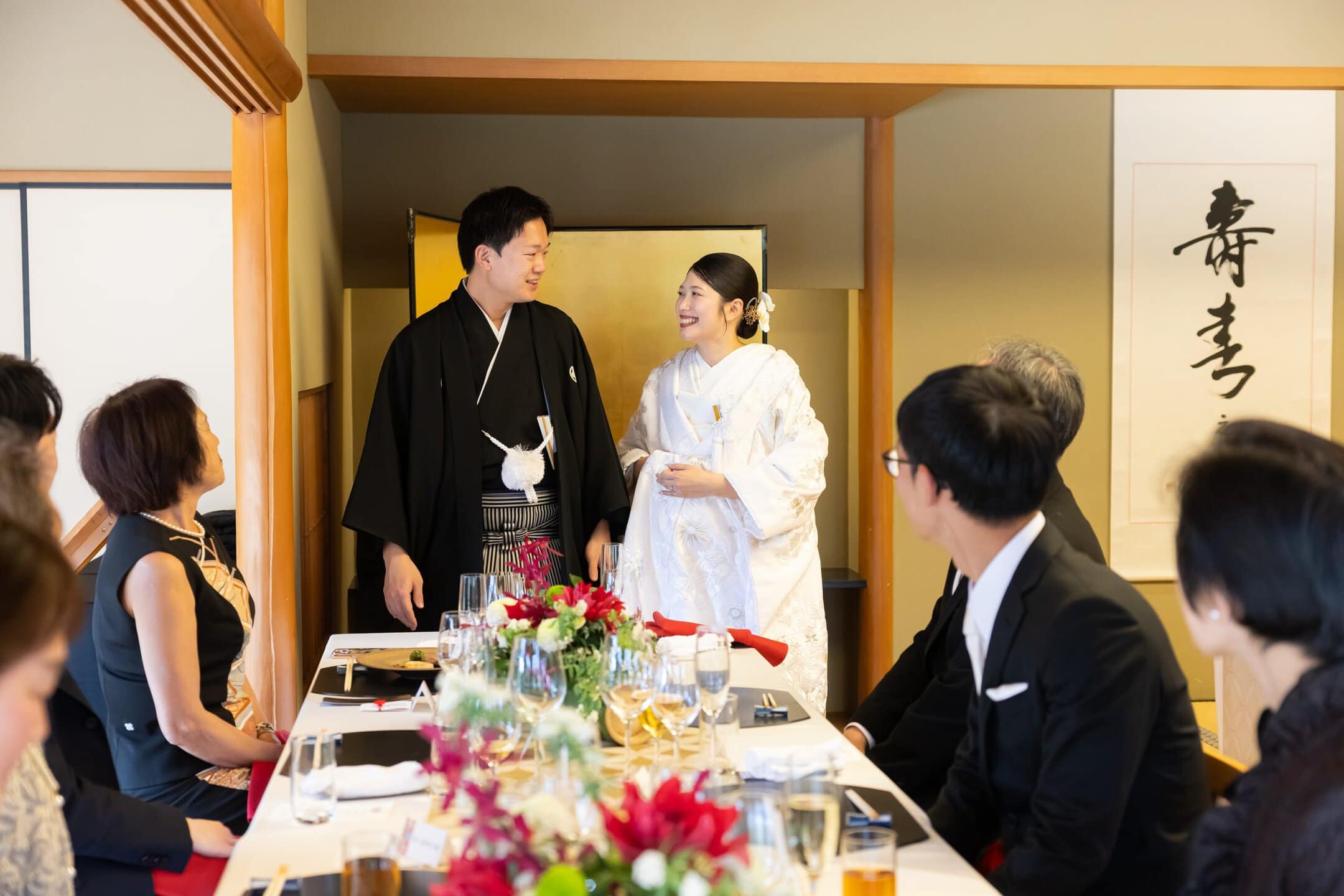 新郎新婦とゲストが和室で祝う伝統的な結婚式の様子。幸せな瞬間を祝福する温かい雰囲気。.