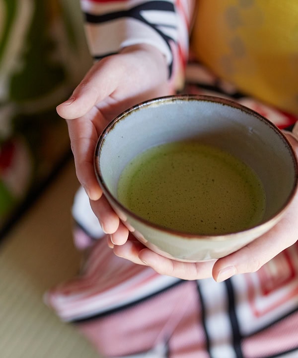 伝統的な抹茶を持つ和装の女性の手元と着物の柄が映える写真.