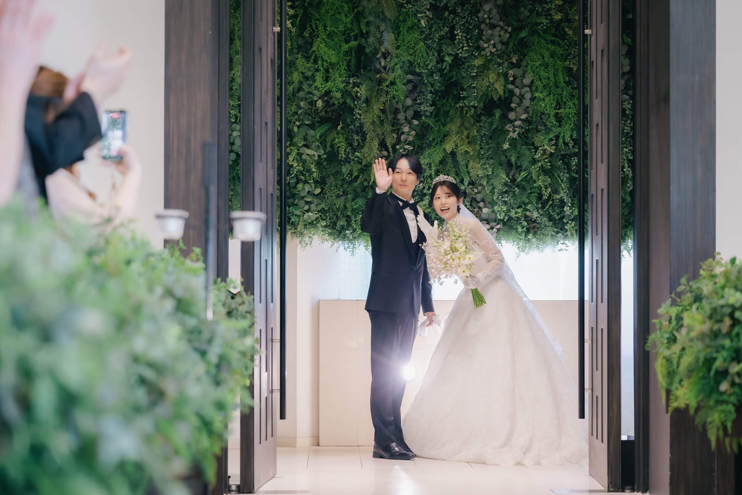 幸せな新郎新婦が緑豊かなウェディング会場で笑顔で手を振る結婚式の瞬間.