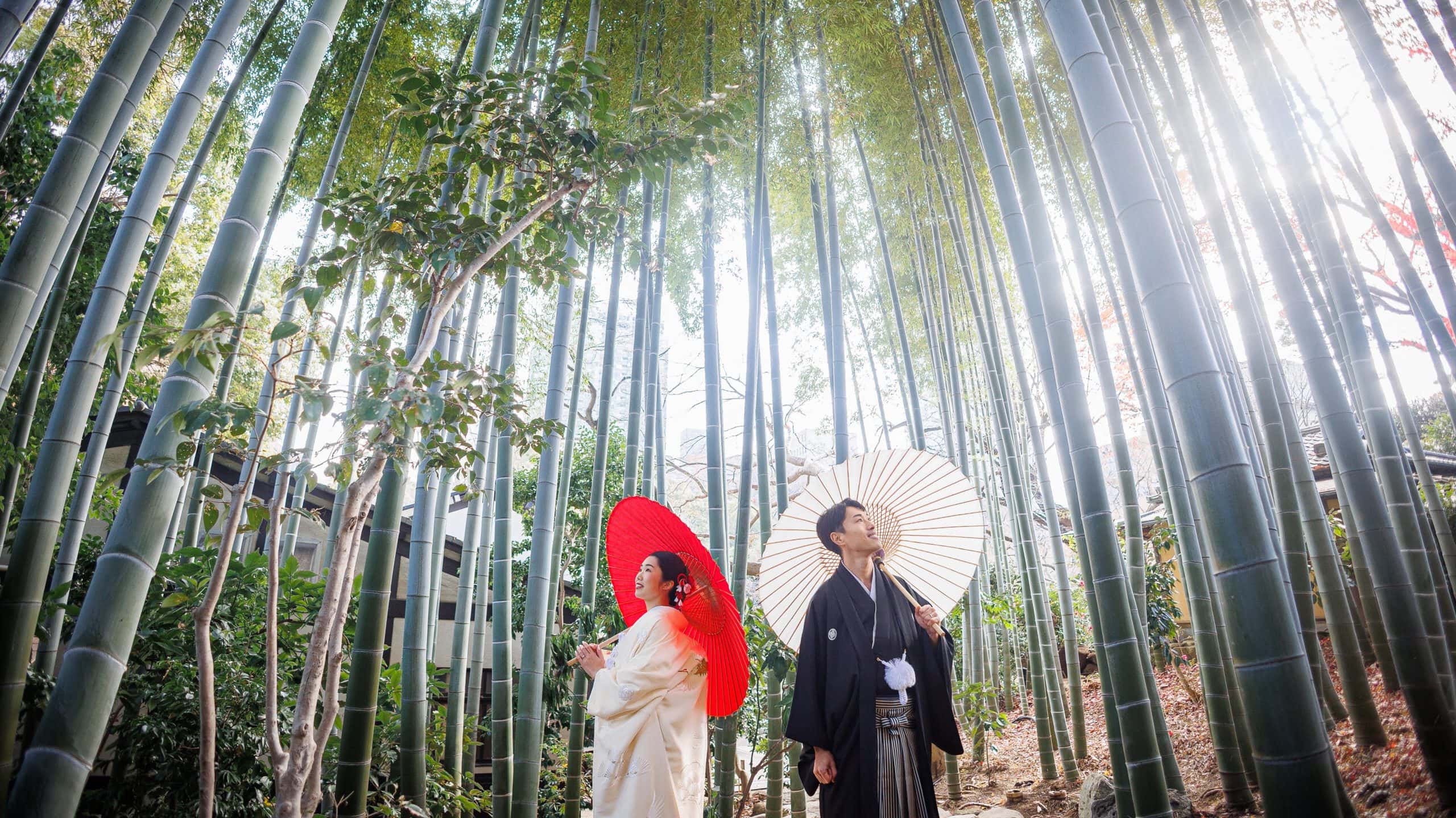 竹林の中で和装の新郎新婦が傘を持ち、結婚式のロマンチックなシーンを演出しています。.