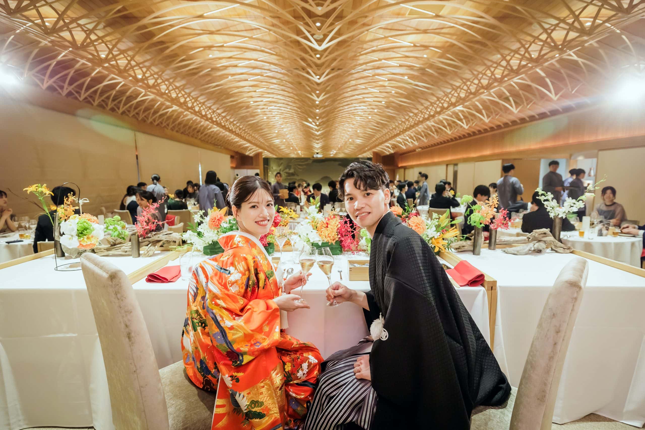 和装と洋装の新郎新婦が結婚式の披露宴で笑顔で乾杯している様子.