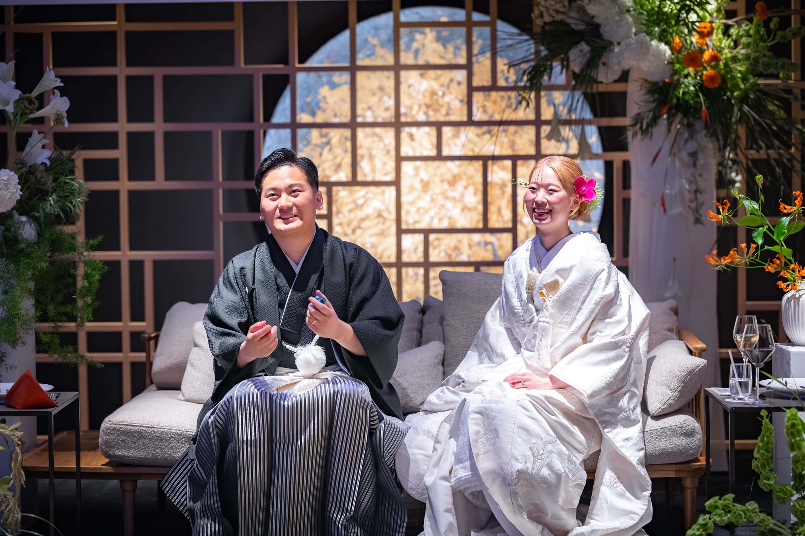和装の新郎新婦が笑顔で座る結婚式の披露宴会場の様子.